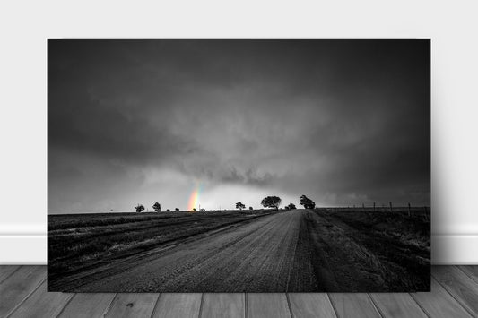 Black and white with color metal print on aluminum of a rainbow appearing under storm clouds down a dusty dirt road on a spring evening in Kansas by Sean Ramsey of Southern Plains Photography.