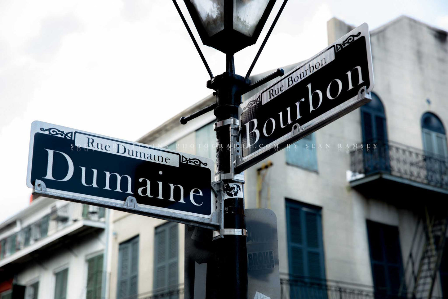 NOLA photography print of street signs on a lamp post at the intersection of Dumaine and Bourbon Street in the New Orleans French Quarter by Sean Ramsey of Southern Plains Photography.