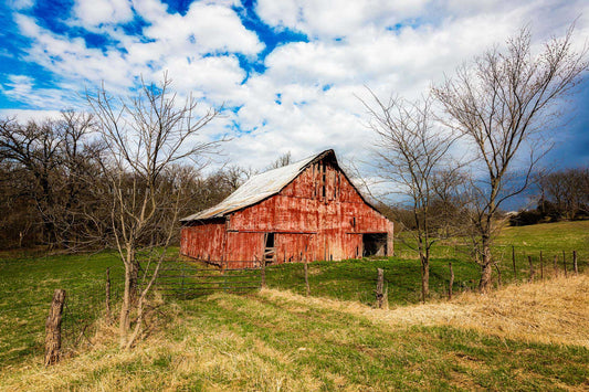 Country photography print of an old red barn with weathered paint nestled between trees on an early spring day in Missouri by Sean Ramsey of Southern Plains Photography.