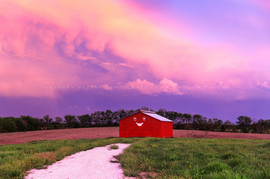 Country photography print of an old red barn with a smiley face under a stormy sky at sunset on a spring evening in Missouri by Sean Ramsey of Southern Plains Photography.