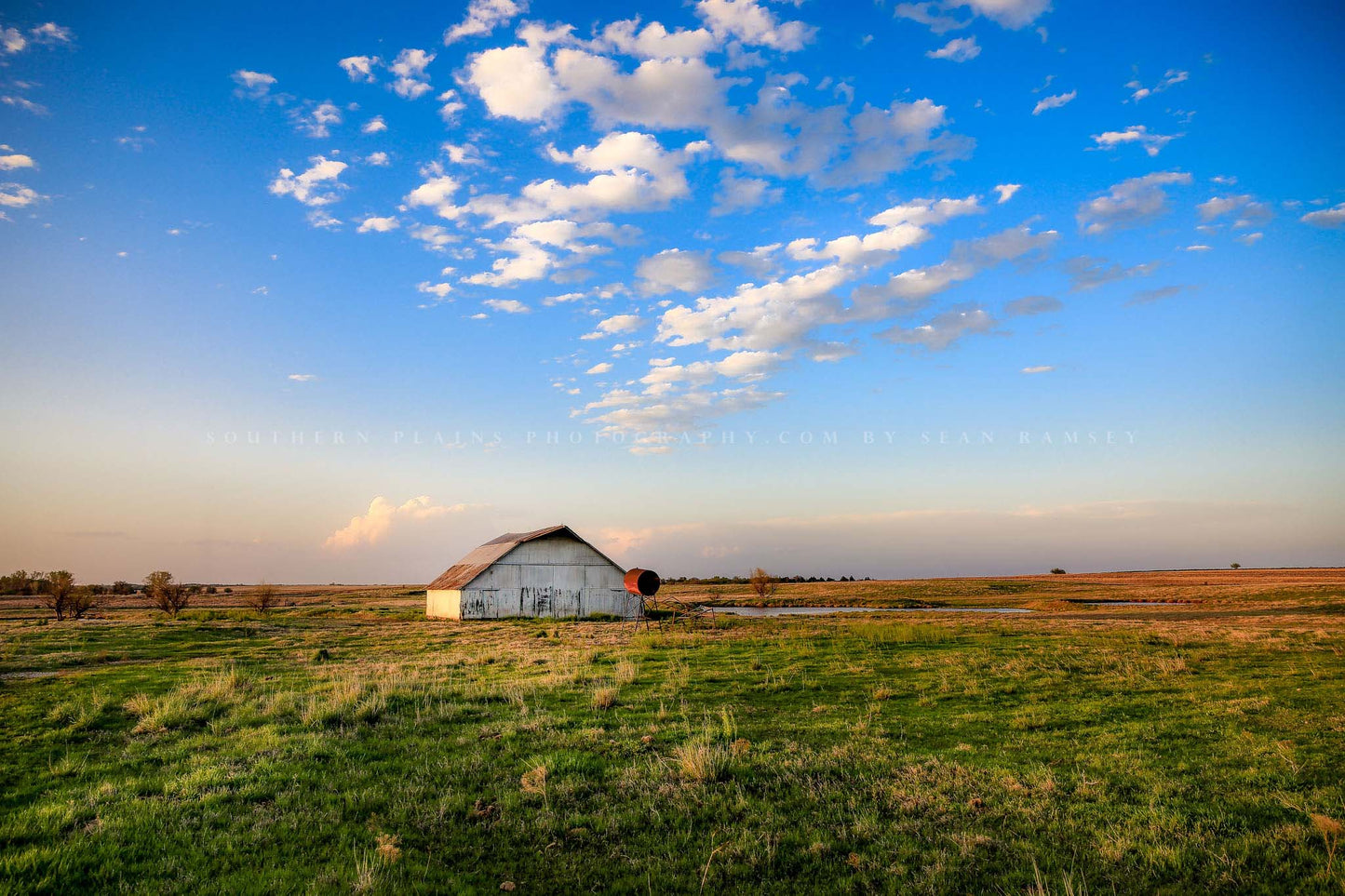 Country photography print of a rustic white barn sitting under a big blue sky on a spring evening in Oklahoma by Sean Ramsey of Southern Plains Photography.