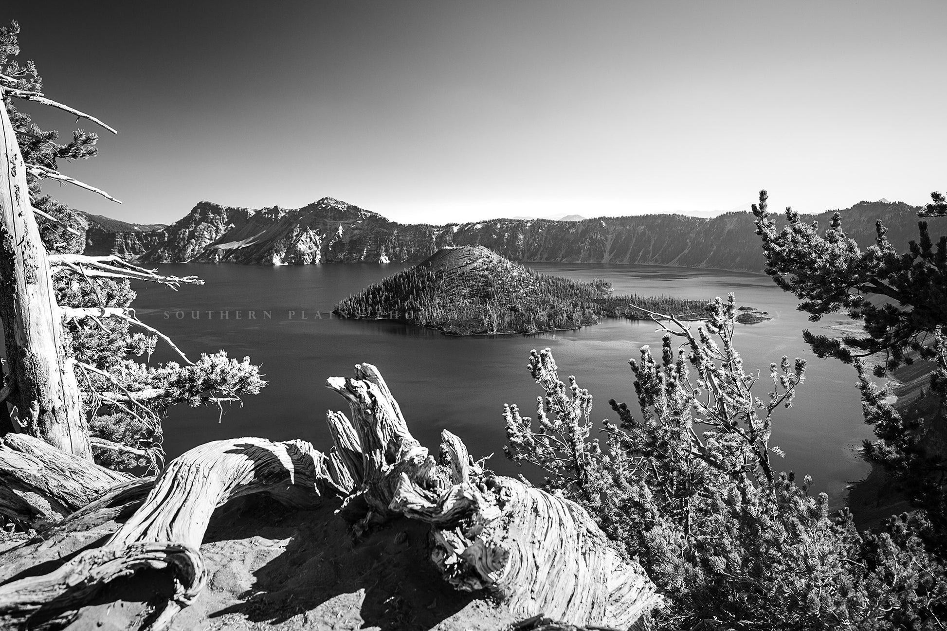 Black and white Pacific Northwest photography print of Wizard Island framed by trees at the rim of Crater Lake at Crater Lake National Park, Oregon by Sean Ramsey of Southern Plains Photography.