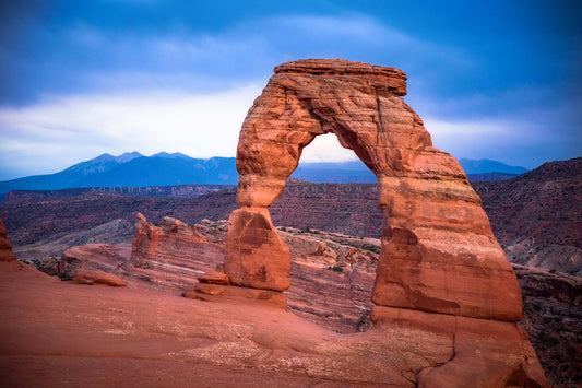 Western landscape photography print of Delicate Arch and the La Sal Mountains on a rainy evening in Arches National Park near Moab, Utah by Sean Ramsey of Southern Plains Photography.