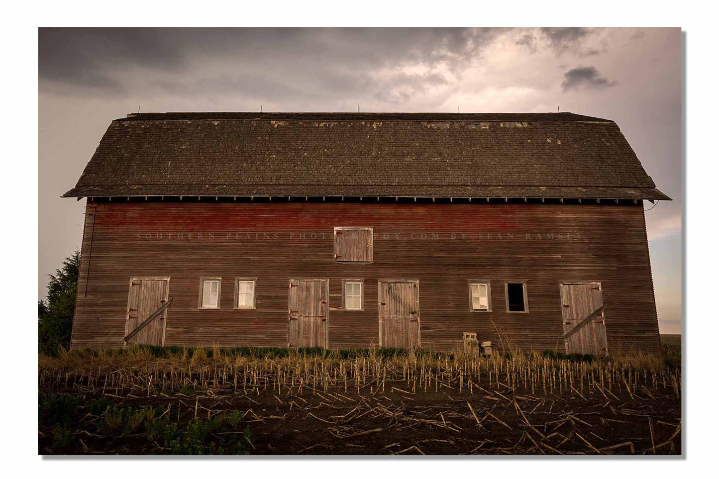 Country photography print of an old red barn side with multiple doors on a stormy day in Nebraska by Sean Ramsey of Southern Plains Photography.