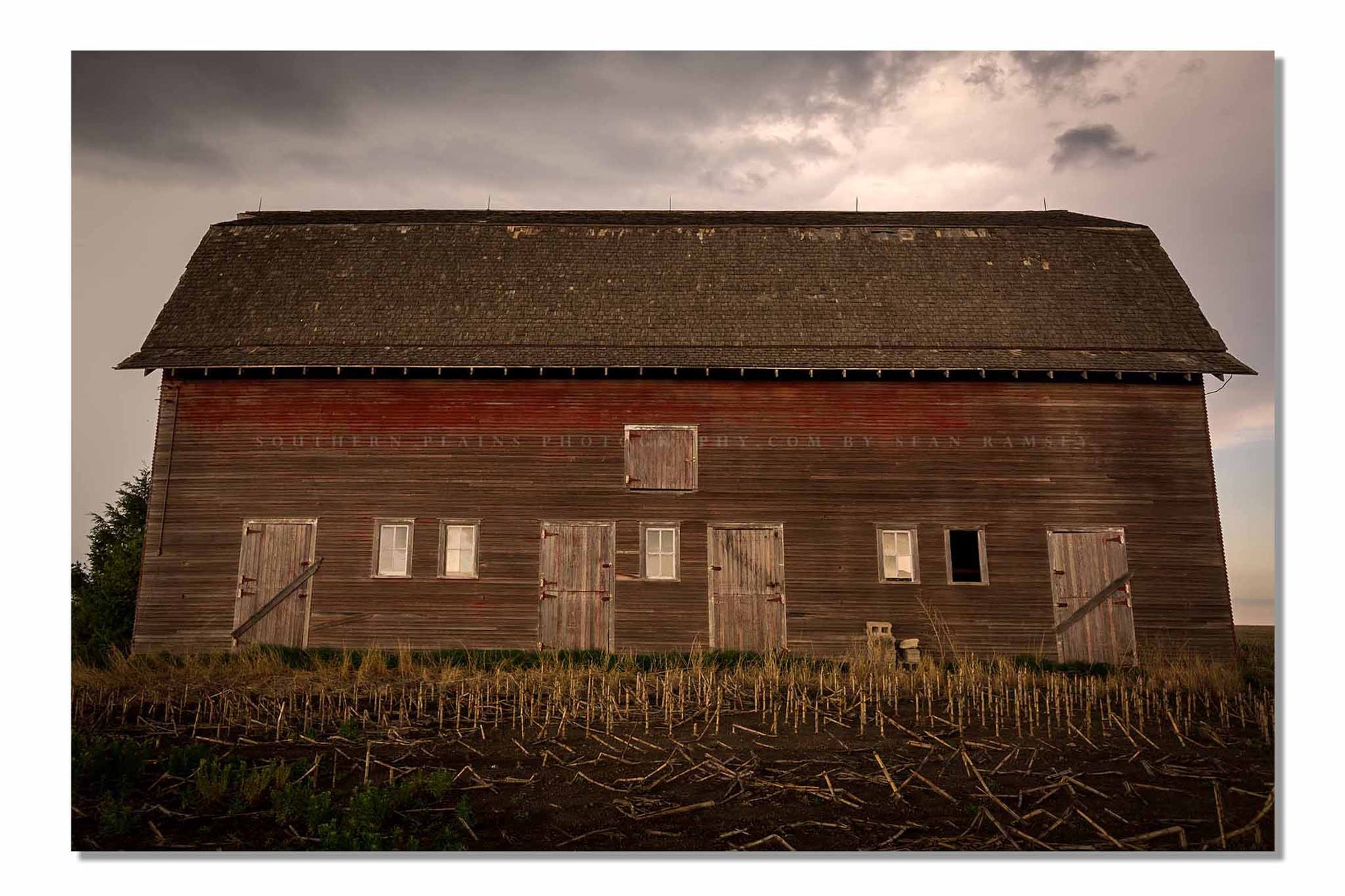 Country photography print of an old red barn side with multiple doors on a stormy day in Nebraska by Sean Ramsey of Southern Plains Photography.