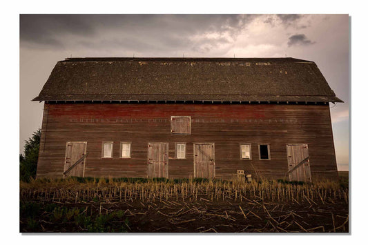 Country photography print of an old red barn side with multiple doors on a stormy day in Nebraska by Sean Ramsey of Southern Plains Photography.