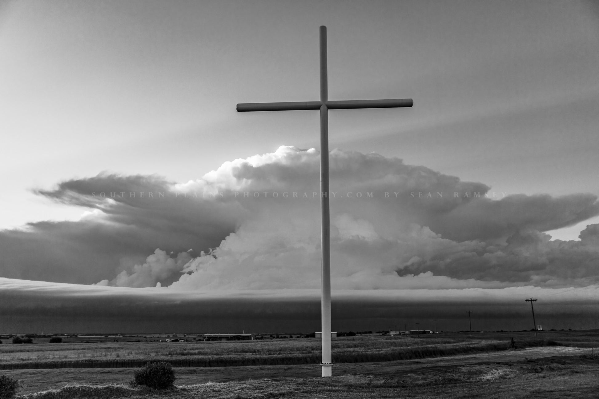 Spiritual photography print of large cross stands in front of a supercell thunderstorm on a stormy spring day in Oklahoma in black and white by Sean Ramsey of Southern Plains Photography.