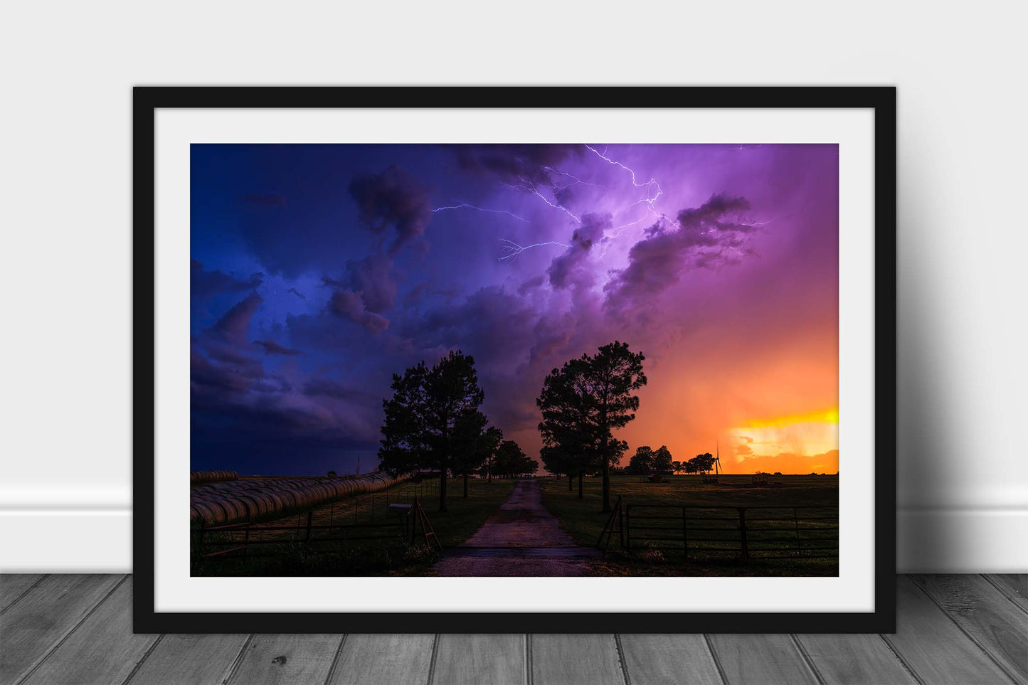 Framed storm print wall art of a dramatic stormy landscape with purple and blue lightning in the sky over a rural path lined with trees at sunset on a spring evening in Oklahoma by Sean Ramsey of Southern Plains Photography.