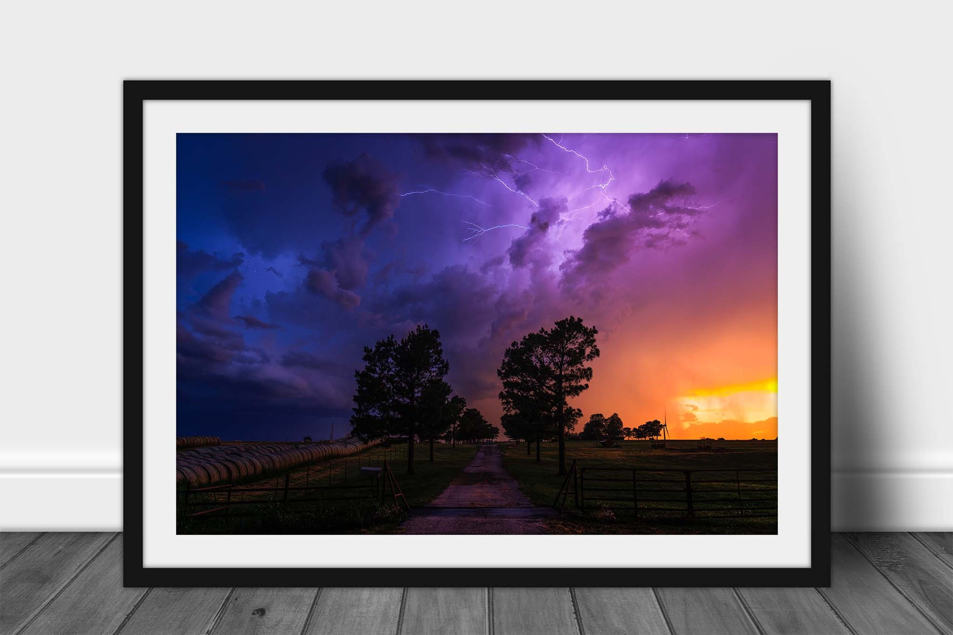 Framed storm print wall art of a dramatic stormy landscape with purple and blue lightning in the sky over a rural path lined with trees at sunset on a spring evening in Oklahoma by Sean Ramsey of Southern Plains Photography.