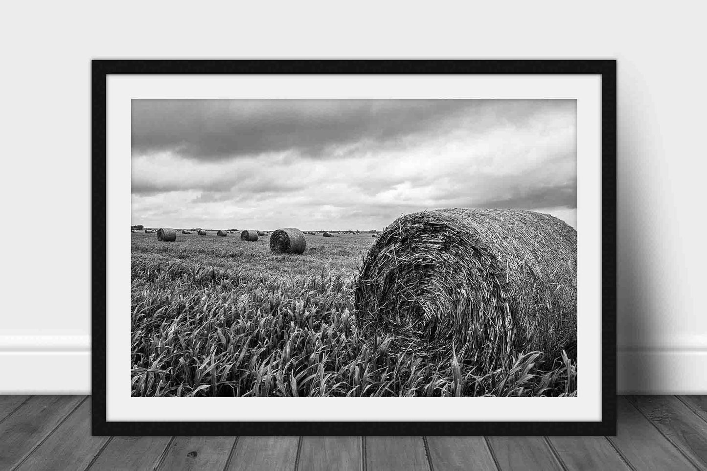 Framed black and white country print of round hay bales in a field of spring wheat on a stormy day in Kansas by Sean Ramsey of Southern Plains Photography.