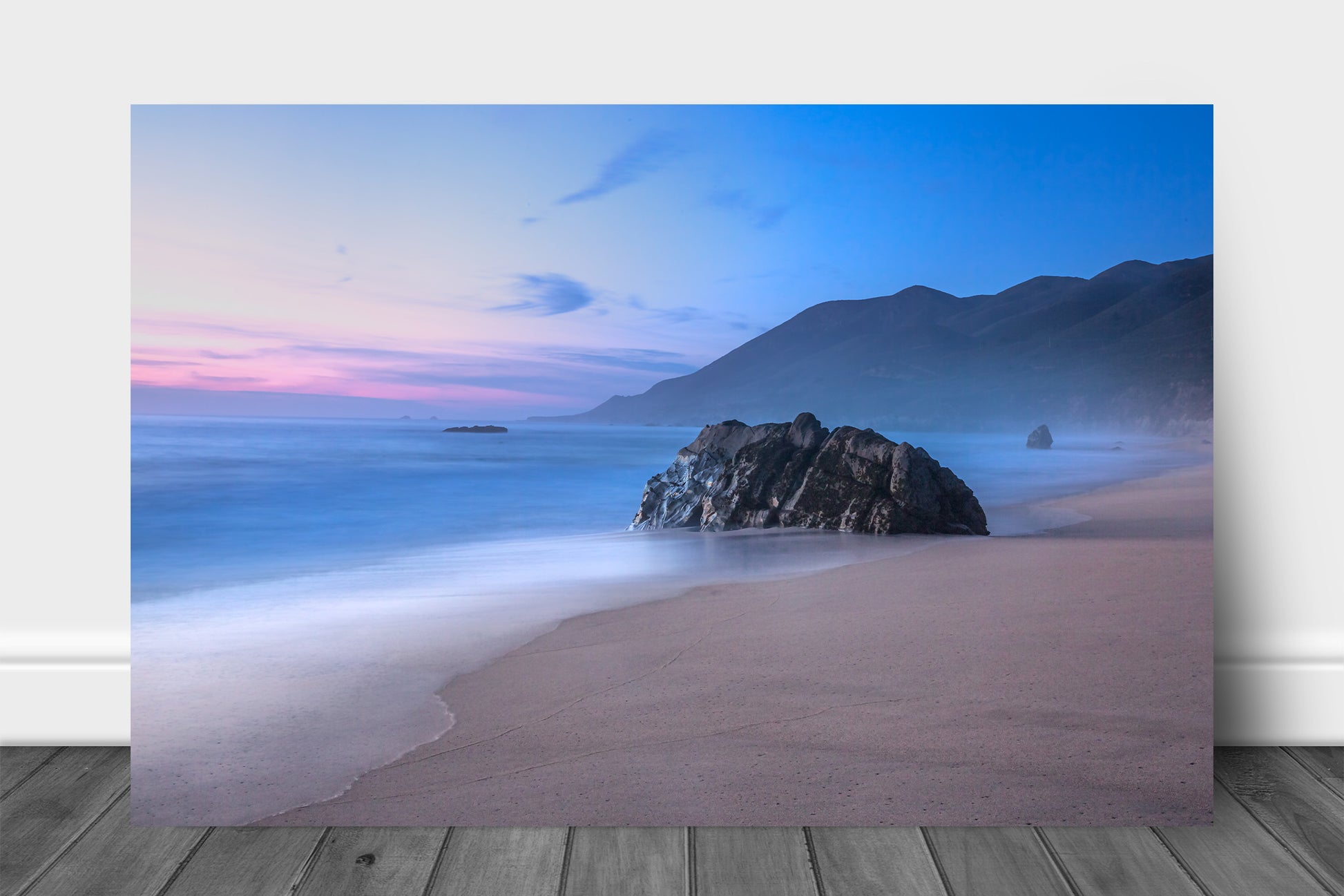 Coastal aluminum metal print wall art of a large boulder on a beach as waves gently wash ashore with mountains in the background during a serene sunset in Big Sur, California by Sean Ramsey of Southern Plains Photography.