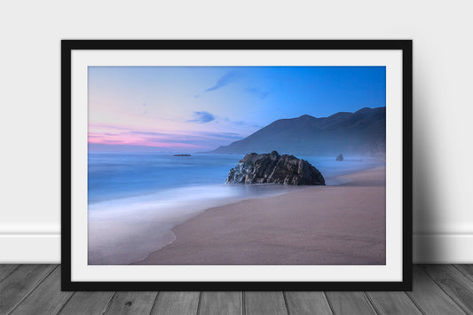 Framed coastal print of a large boulder on a beach as waves gently wash ashore with mountains in the background during a serene sunset in Big Sur, California by Sean Ramsey of Southern Plains Photography.