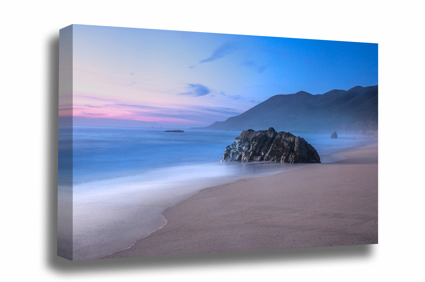 Coastal gallery wrapped canvas wall art of a large boulder on a beach as waves gently wash ashore with mountains in the background during a serene sunset in Big Sur, California by Sean Ramsey of Southern Plains Photography.