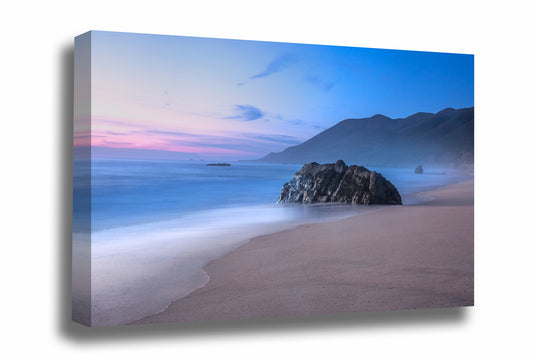 Coastal gallery wrapped canvas wall art of a large boulder on a beach as waves gently wash ashore with mountains in the background during a serene sunset in Big Sur, California by Sean Ramsey of Southern Plains Photography.