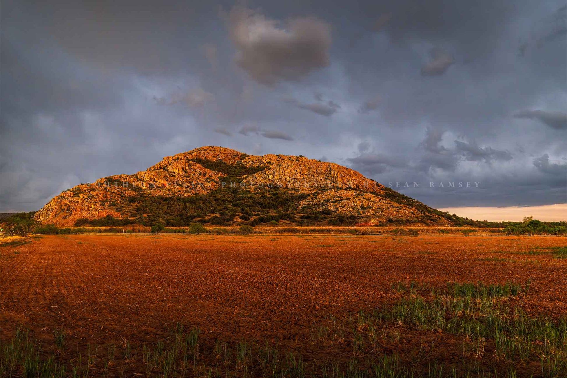 Landscape photography print of the Quartz Mountains rising abruptly over a field as a thunderstorm passes overhead in southwest Oklahoma by Sean Ramsey of Southern Plains Photography.