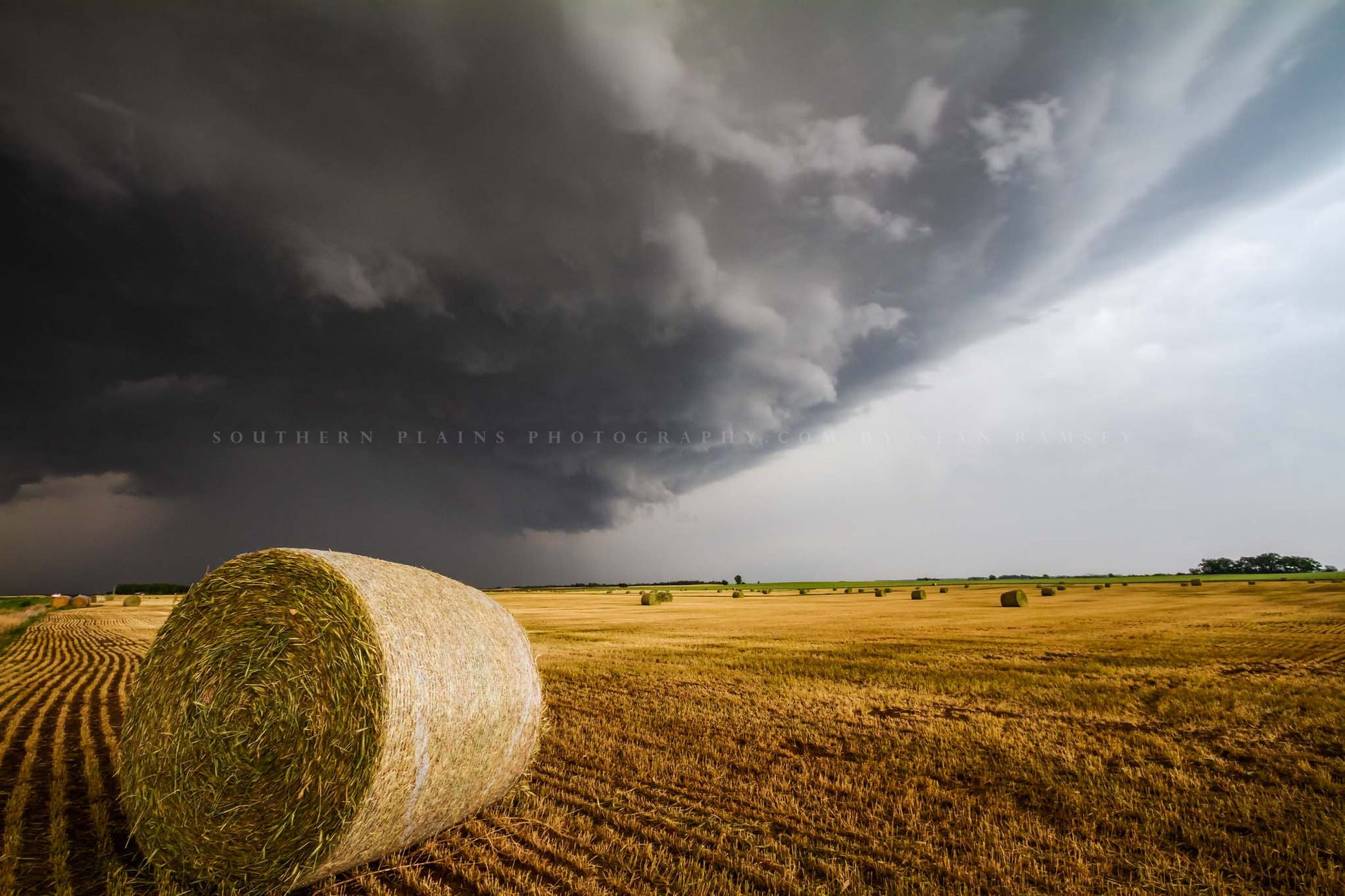 Country photography print of a storm advancing over a golden round hay bale in a field on a stormy spring day in Kansas by Sean Ramsey of Southern Plains Photography.