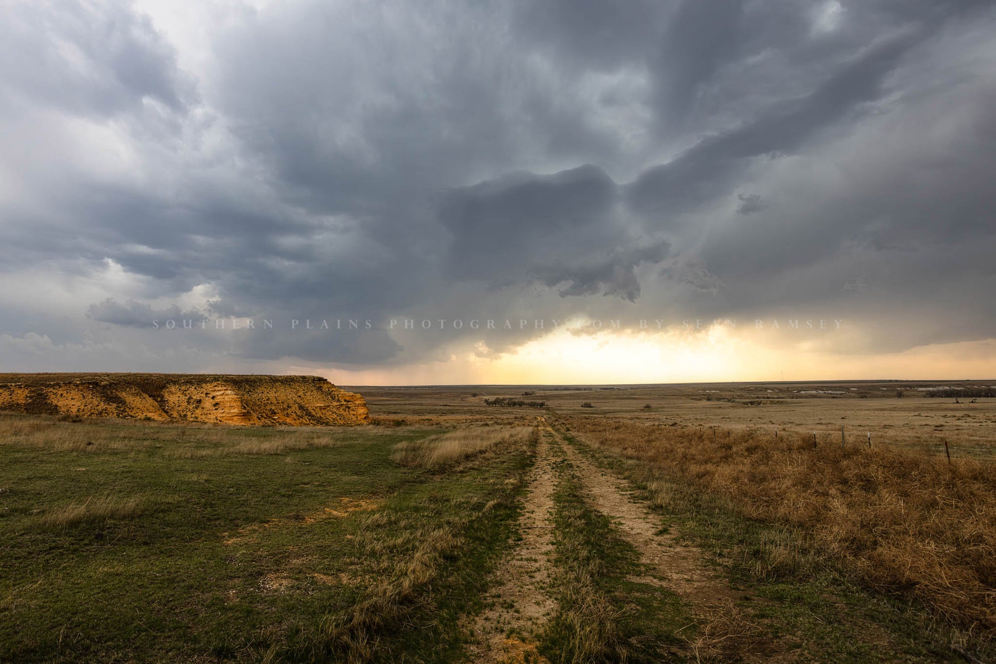 Great Plains photography print of a worn path leading past a bluff to open prairie under a stormy sky on a spring evening in Kansas.