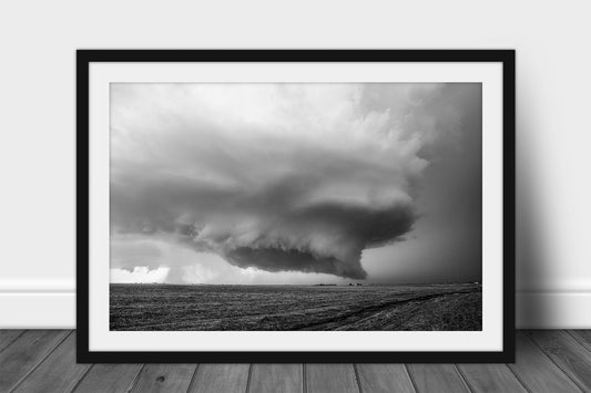 Black and white framed and matted storm print of a supercell thunderstorm with wall cloud hovering over a barren field on a stormy day in Kansas by Sean Ramsey of Southern Plains Photography.