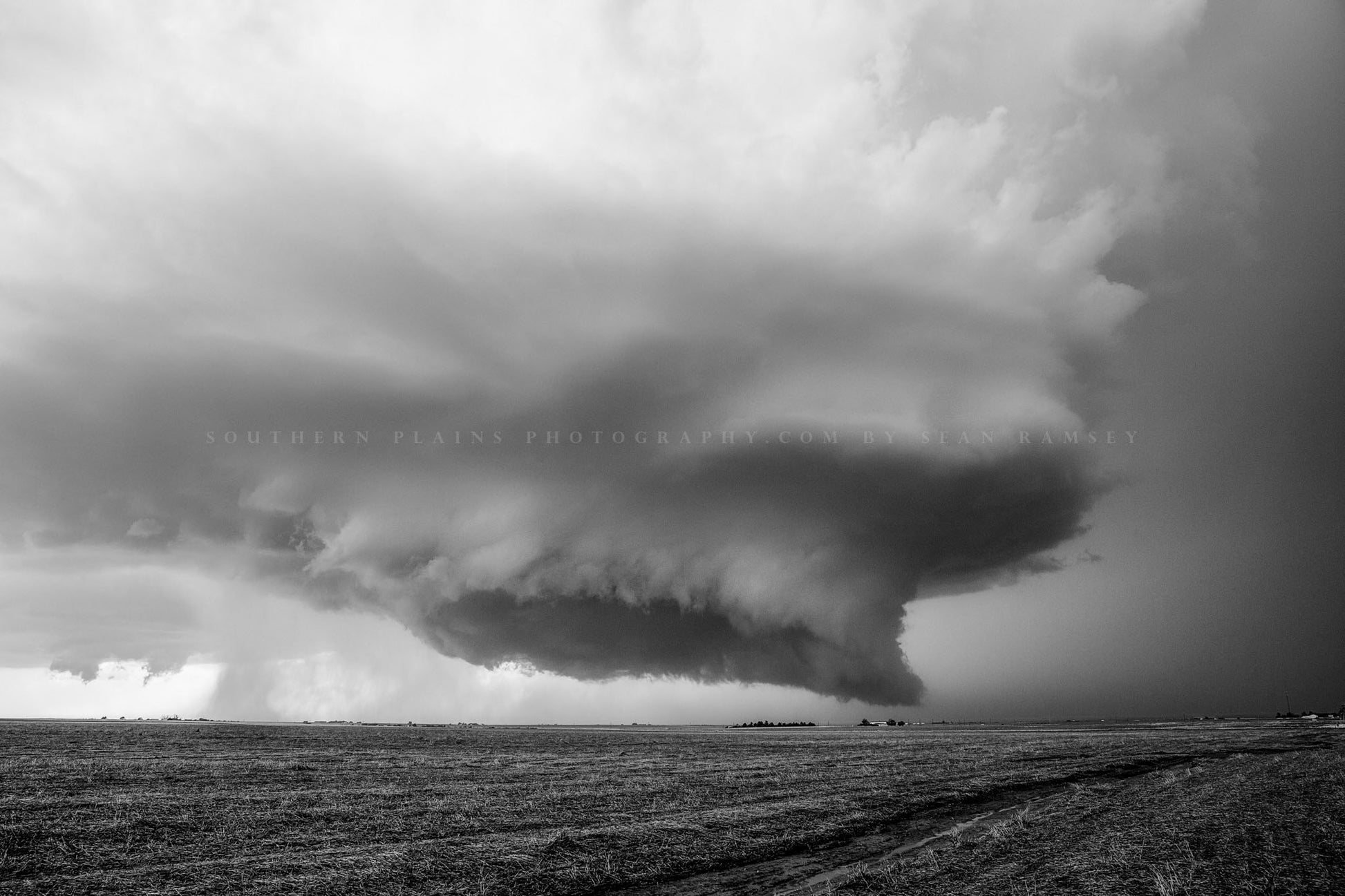 Black and white storm photography print of a supercell thunderstorm with wall cloud lowering toward the ground over a barren field on a stormy spring day in Kansas by Sean Ramsey of Southern Plains Photography.