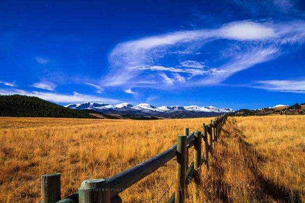 A fence leads to the snow-capped peaks of the Bighorn Mountains under a big blue sky on an autumn day in Wyoming by Sean Ramsey of Southern Plains Photography.
