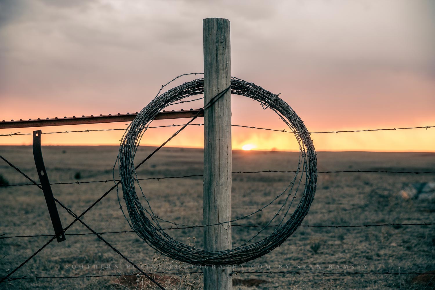 Western photography print of rolled barbed wire on a fence post at sunset on a winter evening in Oklahoma by Sean Ramsey of Southern Plains Photography.