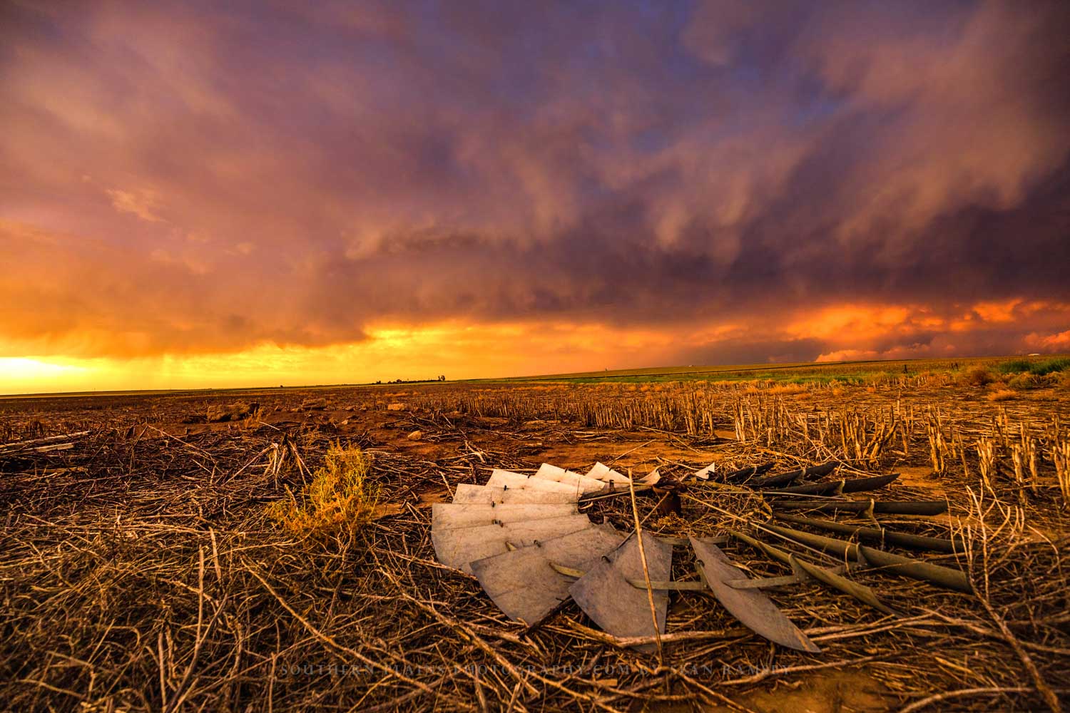 Country photography print of a windmill head laying in a field of corn stubble under a stormy sky at sunset on a spring evening in Kansas by Sean Ramsey of Southern Plains Photography.