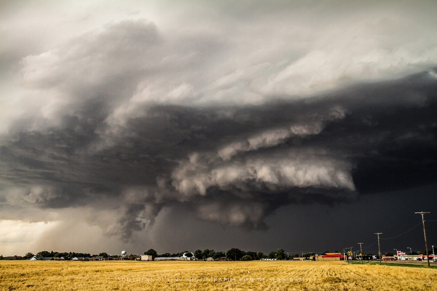 Storm photography print of a supercell thunderstorm with a rotating wall cloud hovering over a small town on a spring day in Oklahoma by Sean Ramsey of Southern Plains Photography.