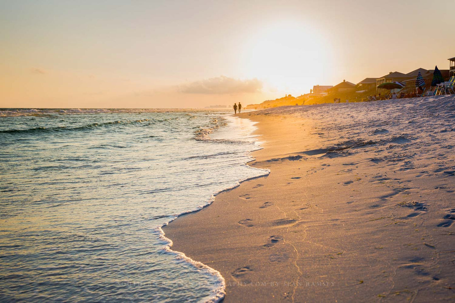 People walk along the beach leaving footprints as waves roll ashore at sunset along the Gulf Coast in Destin, Florida.